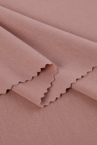 Viscose-covered filament single jersey fabric close-up with folded edge detail and smooth hand feel for base layers and everyday knit garments.