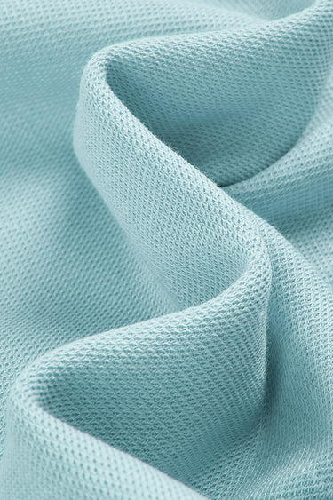 Cotton double piqué knit fabric close-up with curved drape detail and breathable texture for polo shirts and lightweight casual garments.