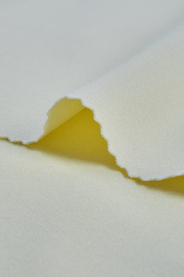 Double-sided piqué knit fabric close-up with edge structure detail and subtle textured surface for refined casualwear.