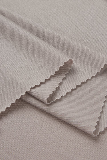 Lenzing TENCEL stretch single jersey fabric close-up with folded edge detail and soft dry touch for warm-weather garments.